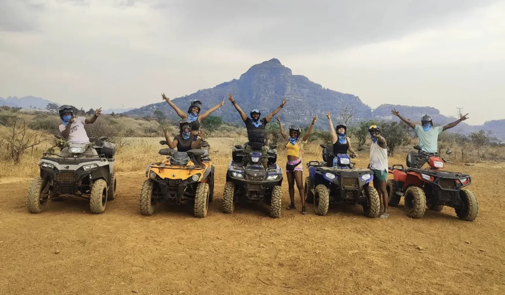 Group of adventurers on ATVs with arms raised against a mountain backdrop