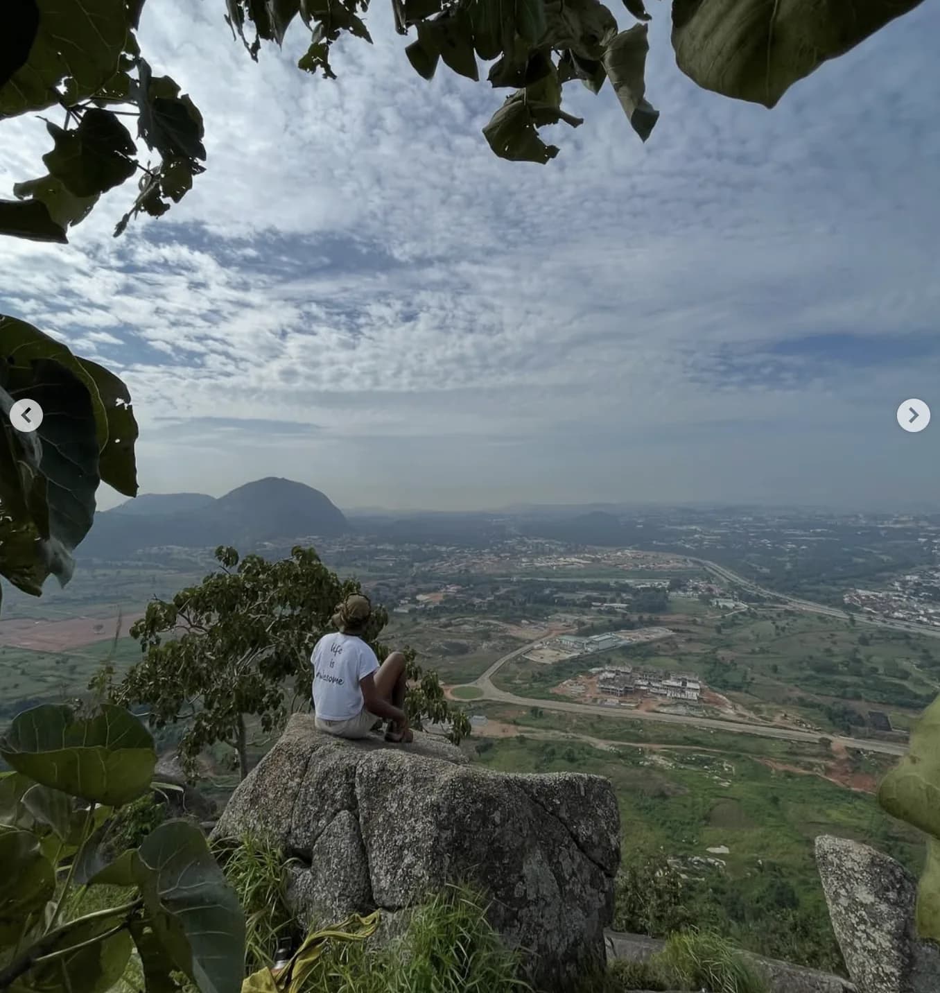 Explorer sitting on a cliff edge overlooking a lush Nigerian valley