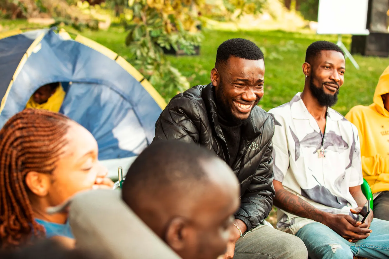 A man in a black jacket laughing with friends beside the tents