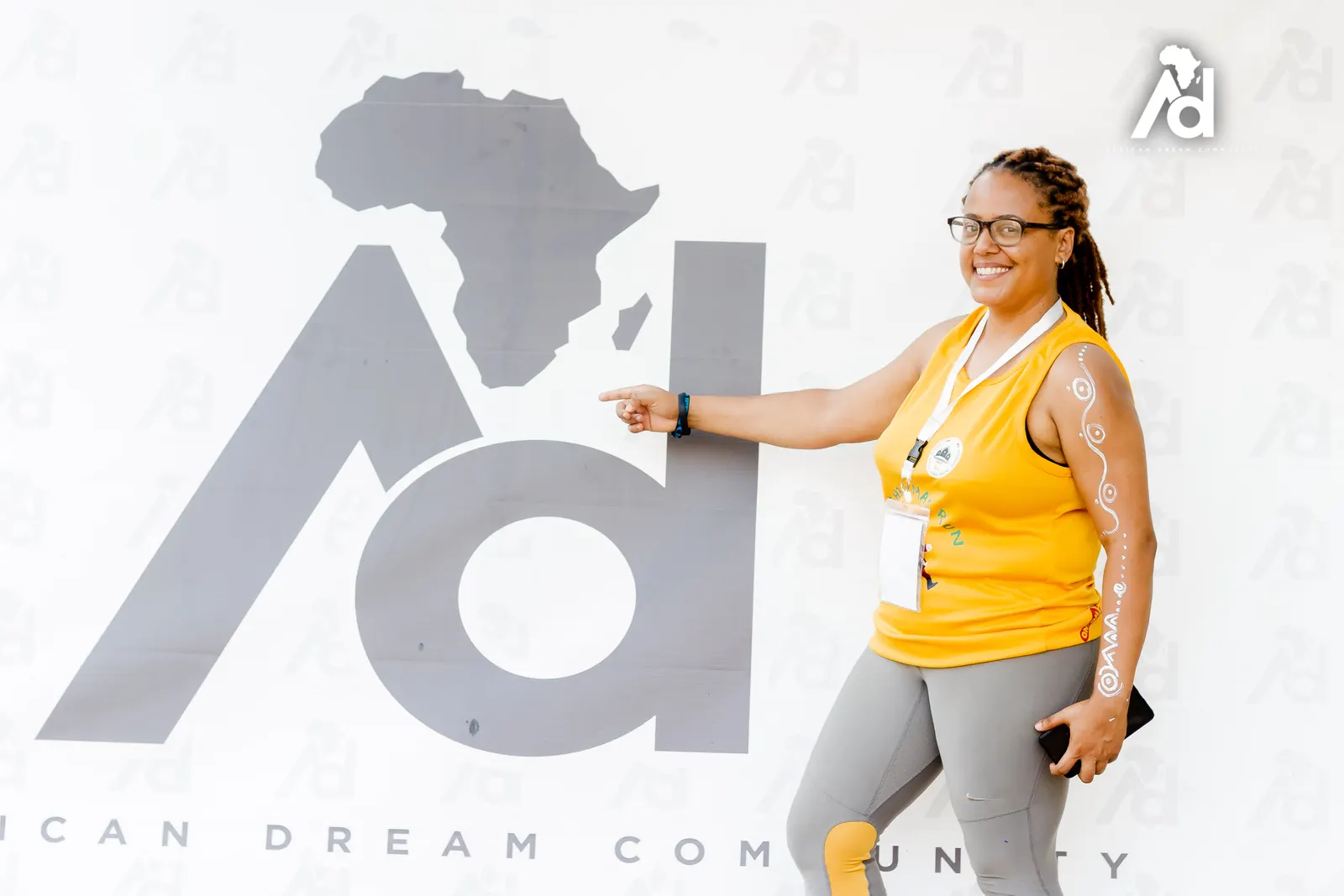 A member smiling and pointing at the African Dream Community logo backdrop