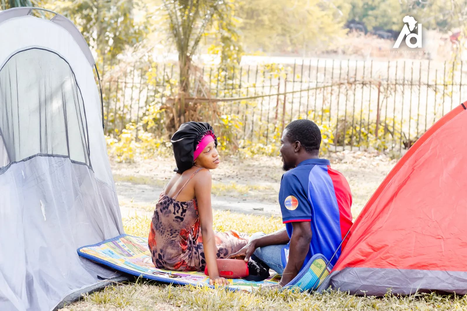Two people sitting on a mat beside their tent, talking