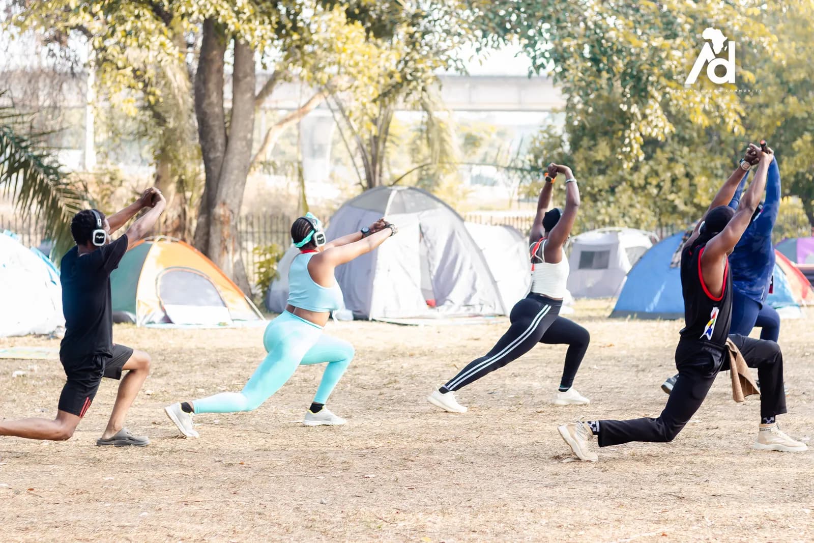Members stretching in an outdoor workout, tents pitched behind them