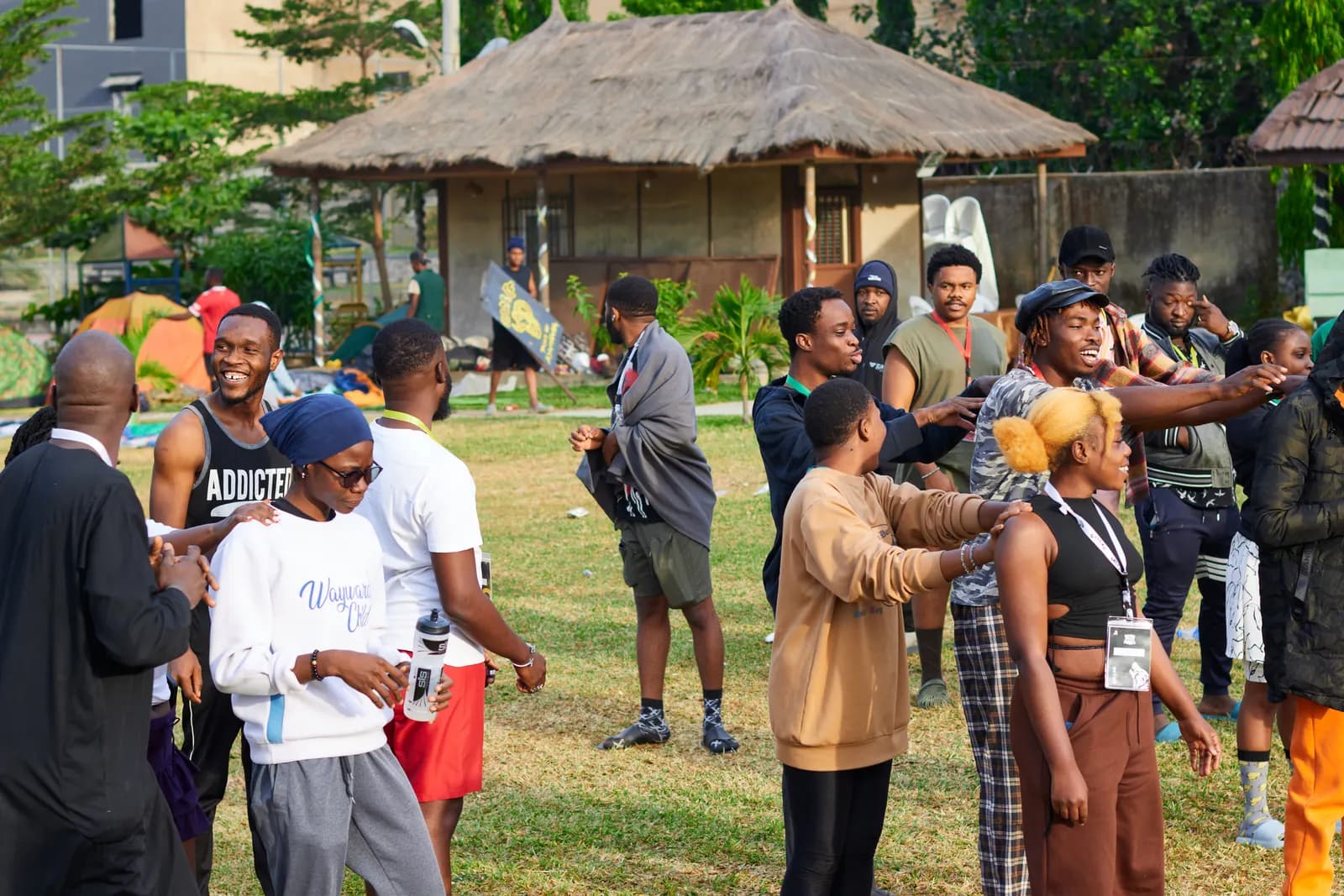 Community members chatting in small groups on a lawn by thatched huts