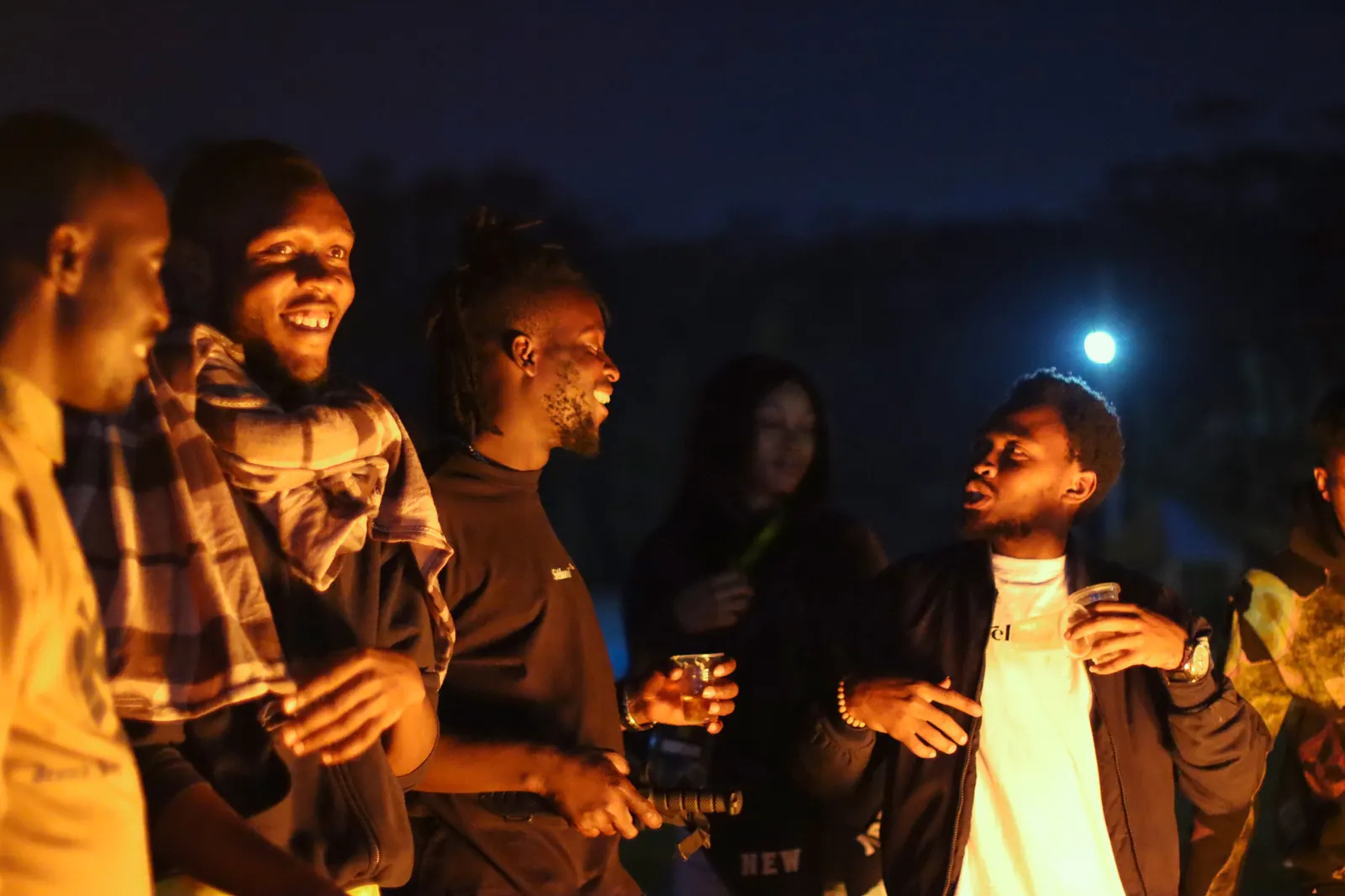 Friends laughing together around a fire at night, lit by the flames